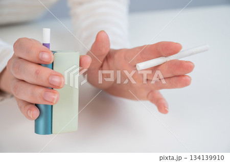 Woman holding regular and electronic cigarette on white background. Tobacco heating systems. Woman holding regular and electronic cigarette on white background. Tobacco heating systems. 134139910