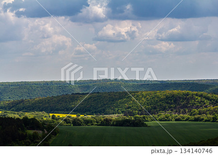 Lush green landscape under a cloudy sky with rolling hills valleys and vibrant foliage Lush green landscape under a cloudy sky with rolling hills valleys and vibrant foliage 134140746