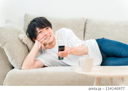 ソファーに横になりテレビを見る若いアジア人男性 134140977