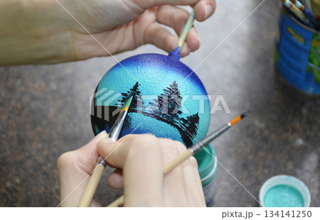Female hands carefully painting a Christmas ball in vibrant blue hues 134141250
