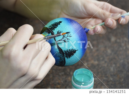 Female hands carefully painting a Christmas ball in vibrant blue hues 134141251