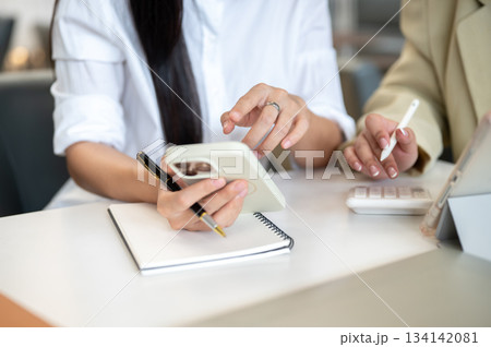 Close up woman student holding pen showing phone over notebook on table to a teacher or supervisor. Close up woman student holding pen showing phone over notebook on table to a teacher or supervisor. 134142081