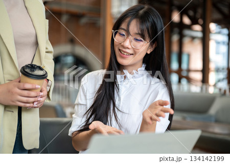 Asian woman student with eyeglasses showing a work on laptop to teacher while sitting at cafe table Asian woman student with eyeglasses showing a work on laptop to teacher while sitting at cafe table 134142199