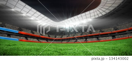 Grass pitch is spanning stadium with curved roof lit by floodlights with tiered red blue seating 134143002