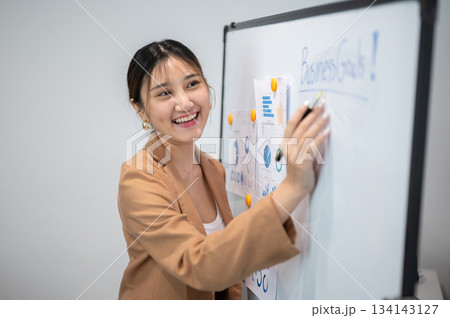Asian businesswoman office worker holding a pen under chain looking at laptop on table in white room Asian businesswoman office worker holding a pen under chain looking at laptop on table in white room 134143127