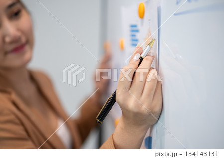 Asian businesswoman office worker holding a pen under chain looking at laptop on table in white room Asian businesswoman office worker holding a pen under chain looking at laptop on table in white room 134143131