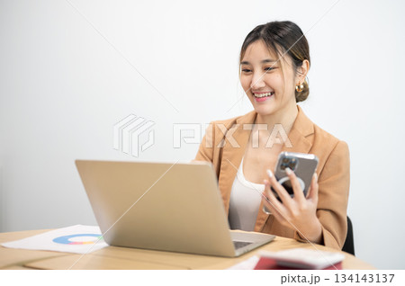 Asian businesswoman office worker holding a pen under chain looking at laptop on table in white room 134143137
