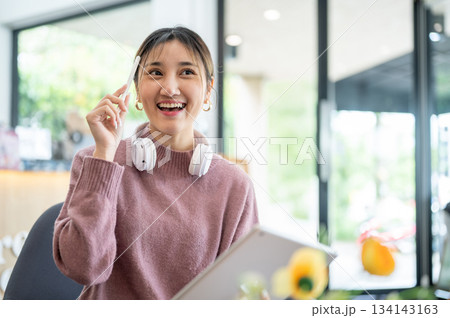 Asian businesswoman office worker holding a pen under chain looking at laptop on table in white room 134143163