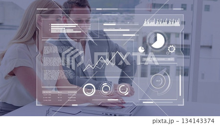 Colleagues in business attire analyzing data and typing on laptop in office, with HUD display 134143374