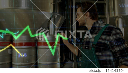 Worker in brewery wearing green apron analyzing brew, kegs and tanks, pipes, digital graph overlay Worker in brewery wearing green apron analyzing brew, kegs and tanks, pipes, digital graph overlay 134143504