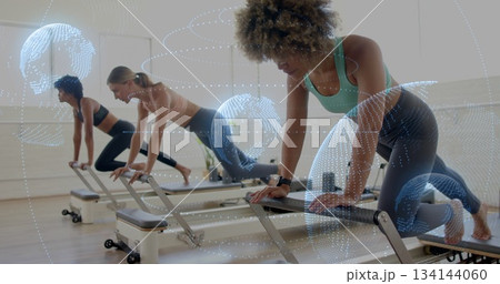 Women in sportswear gripping reformer bars driving carriage engaging abs in gym with orbit overlay Women in sportswear gripping reformer bars driving carriage engaging abs in gym with orbit overlay 134144060