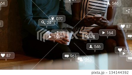 Sitting friends holding smartphone and coffee cup in cafe, floating social notification icons Sitting friends holding smartphone and coffee cup in cafe, floating social notification icons 134144392