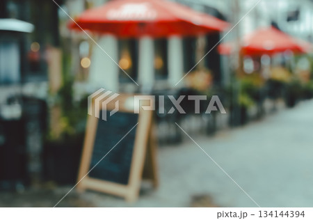 Blurry abstract image of urban street with outdoor cafe seating and red umbrellas background Blurry abstract image of urban street with outdoor cafe seating and red umbrellas background 134144394