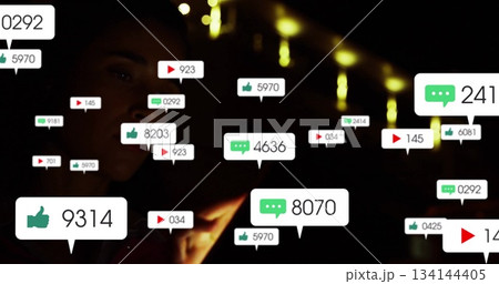 Holding smartphone woman wearing dark clothing viewing floating media icons in dim room, copy space 134144405