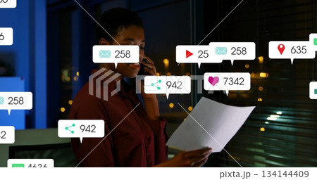 Wearing button-up shirt, analyzing smartphone and document with notifications in office at night Wearing button-up shirt, analyzing smartphone and document with notifications in office at night 134144409