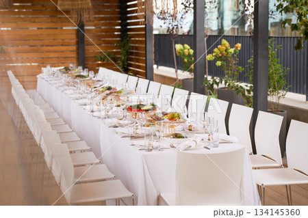 Wide shot of long set table on terrace with city view - elegant table setting for event Wide shot of long set table on terrace with city view - elegant table setting for event 134145360