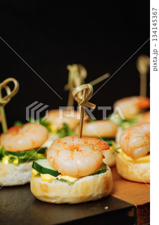 Close-up of canape with shrimp and cucumber on dark background - elegant appetizer 134145367