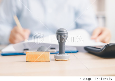 Businessperson stamping document on clipboard at office desk, concept of contract approval, legal authorization, business agreement validation or administrative paperwork process. stamp approval. Businessperson stamping document on clipboard at office desk, concept of contract approval, legal authorization, business agreement validation or administrative paperwork process. stamp approval. 134146515