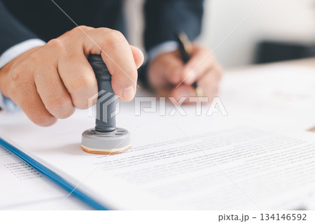 Businessman signing and stamping official document at desk, concept of legal contract approval, authorization or business agreement confirmation in corporate office background. stamp approval Businessman signing and stamping official document at desk, concept of legal contract approval, authorization or business agreement confirmation in corporate office background. stamp approval 134146592