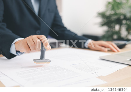 Businessman signing and stamping official document at desk, concept of legal contract approval, authorization or business agreement confirmation in corporate office background. stamp approval 134146594
