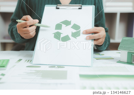 Business person holding recycle symbol on clipboard with green charts on desk, representing circular economy, eco responsibility, sustainability and environmental business concept. Business person holding recycle symbol on clipboard with green charts on desk, representing circular economy, eco responsibility, sustainability and environmental business concept. 134146627