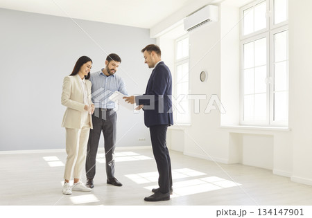 Young happy couple reaching agreement and going to sign a deal with a real estate agent. 134147901