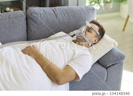 Man resting on sofa with CPAP oxygen mask for sleep apnea therapy at home Man resting on sofa with CPAP oxygen mask for sleep apnea therapy at home 134148340