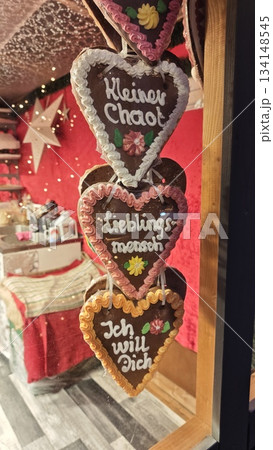 This festive photo captures a set of traditional German gingerbread hearts (Lebkuchenherzen) hanging in a Christmas market stall. Decorated with colorful icing and loving messages in German 134148545