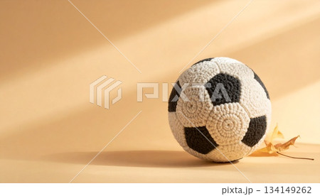 毛糸の編み目が細かく見える手編みウールのサッカーボールを、暖かいキャラメル色のマット背景に配置した静 毛糸の編み目が細かく見える手編みウールのサッカーボールを、暖かいキャラメル色のマット背景に配置した静 134149262