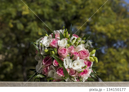Wedding bouquet resting on stone surface with blurred foliage background 134150177