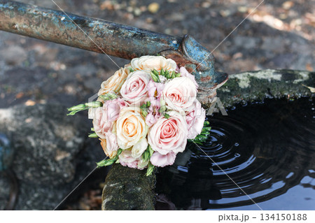 Wedding bouquet resting on an old fountain, pastel roses and eustoma flowers creating a romantic atmosphere Wedding bouquet resting on an old fountain, pastel roses and eustoma flowers creating a romantic atmosphere 134150188