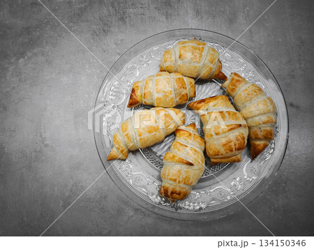 Freshly baked croissants arranged on elegant glass plate on gray background 134150346