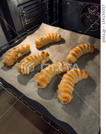 Veal sausage rolls in puff pastry baking in oven on baking paper Veal sausage rolls in puff pastry baking in oven on baking paper 134150357