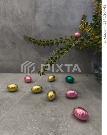 Chocolate easter eggs scattered on a table with mimosa flowers celebrating spring copy space gray background Chocolate easter eggs scattered on a table with mimosa flowers celebrating spring copy space gray background 134150445