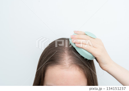 Woman using scalp massager to stimulate hair growth and care for scalp health, copy space. Concept of beauty treatment, wellness, and addressing alopecia and thinning hair through daily routines. 134151237