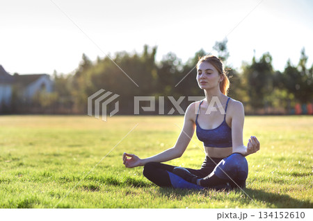Young sportive woman in yoga position meditates in field at sunrise. Young sportive woman in yoga position meditates in field at sunrise. 134152610