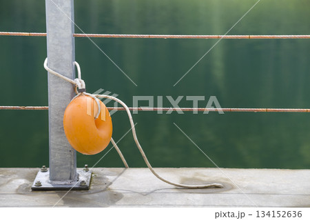 Yellow plastic buoy attached to a metal fence on the bank of a lake with green water. Yellow plastic buoy attached to a metal fence on the bank of a lake with green water. 134152636