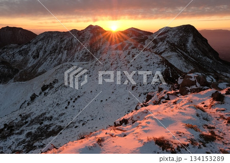 雪山の稜線に昇る朝日　光芒が雪面を照らす冬の山岳風景 134153289