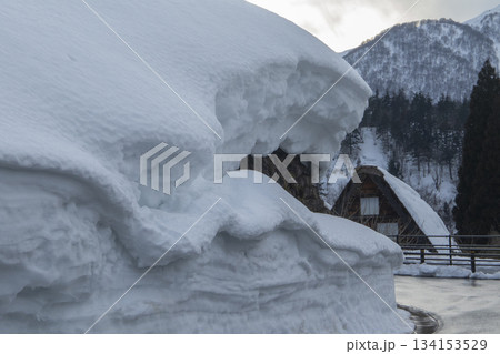 巨大な雪の壁と奥に見える合掌造り民家の遠景 巨大な雪の壁と奥に見える合掌造り民家の遠景 134153529