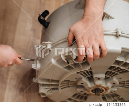 Mechanic repairing a washing machine drum, showing hands-on appliance maintenance at work. 134153563