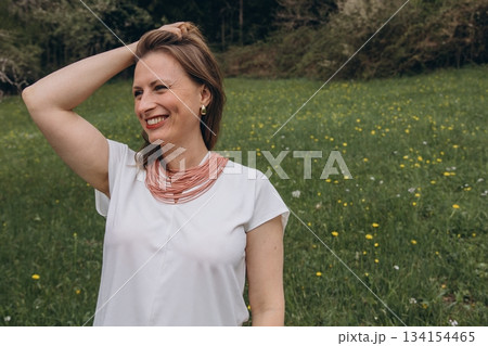Smiling middle aged woman stands near blooming tree in spring garden. Natural beauty, joy, and harmony with nature. Seasonal renewal, inner peace, and emotional wellness Smiling middle aged woman stands near blooming tree in spring garden. Natural beauty, joy, and harmony with nature. Seasonal renewal, inner peace, and emotional wellness 134154465