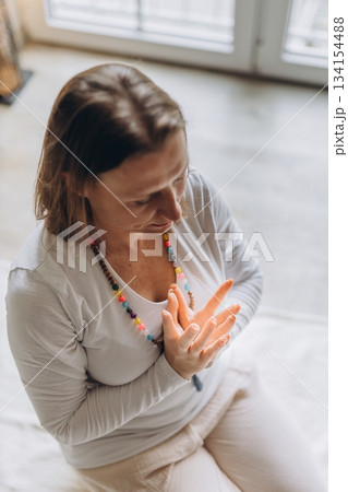 Calm woman practicing kundalini yoga at home in prayer pose. Mindfulness, inner peace, and healthy lifestyle in serene morning light Calm woman practicing kundalini yoga at home in prayer pose. Mindfulness, inner peace, and healthy lifestyle in serene morning light 134154488
