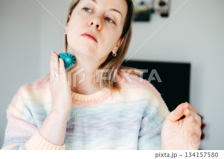 A woman uses a spiked massage ball on her neck to relieve tension. Self-massage technique, neck pain relief, ergonomic self-care, myofascial release. A woman uses a spiked massage ball on her neck to relieve tension. Self-massage technique, neck pain relief, ergonomic self-care, myofascial release. 134157580