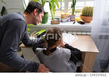 A schoolgirl girl studies with a tutor at home, additional lesson preparation, dad helps his daughter with lessons 134157812