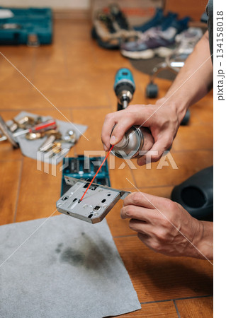 Vertical shot of carpenter male lubricating door lock mechanism with spray oil, performing home maintenance or diy repair work to prevent sticking and extend hardware lifespan in domestic setting. 134158018