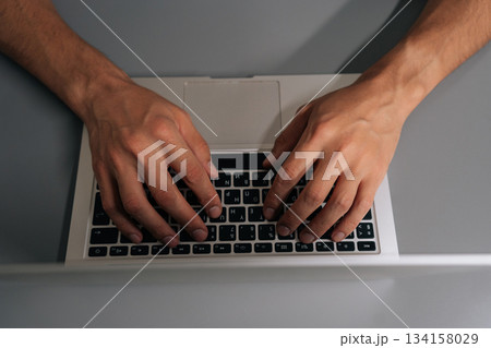 Close-up hands of unrecognizable businessman typing on laptop keyboard, professional home office scene showing remote work, coding, online learning, business tasks and digital communication. 134158029