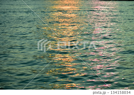 Reflection of city light on water at night. Night sea view with street light. Light hitting on the ocean.Sea background. Background of the calm water, water waves. Sea water surface. 134158034