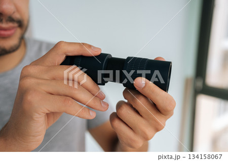 Close-up of voyeur male curiously peering out window using monocular, watching with intense emotion. Engaging in voyeurism. Observing surveillance. Peeping through curtains. Maintaining vigilance. Close-up of voyeur male curiously peering out window using monocular, watching with intense emotion. Engaging in voyeurism. Observing surveillance. Peeping through curtains. Maintaining vigilance. 134158067