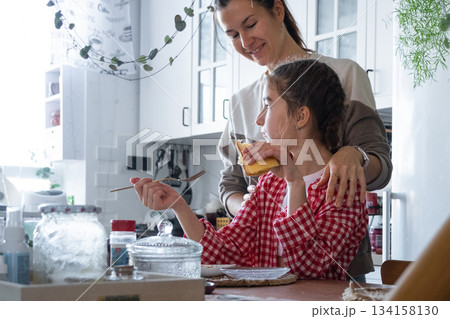 The girl has breakfast in the kitchen in the morning at the table in the company of her mother, morning preparations 134158130