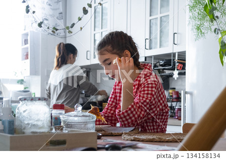The girl has breakfast in the kitchen in the morning at the table in the company of her mother, morning preparations The girl has breakfast in the kitchen in the morning at the table in the company of her mother, morning preparations 134158134